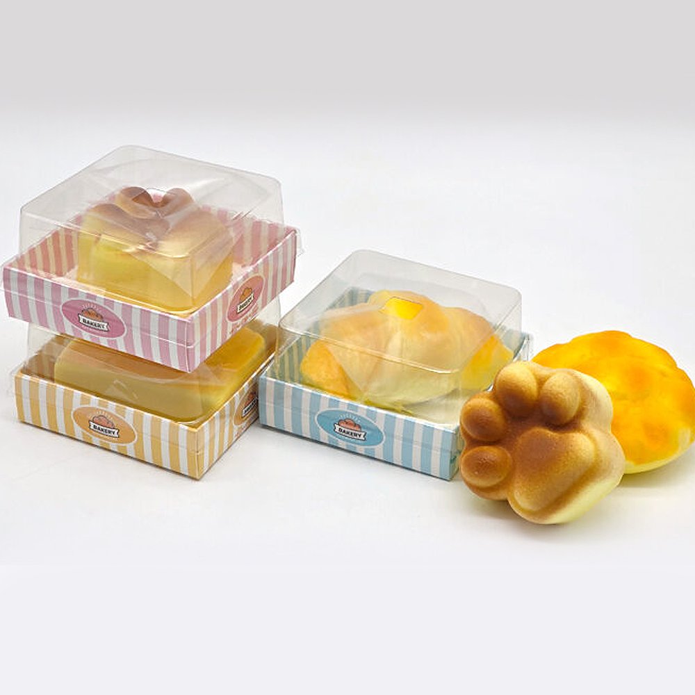 Individual clear bakery gift boxes containing butter toast, croissant, and cat paw bread squishies laid out on a white background, ideal party favor goodie bag filler and holiday gift set