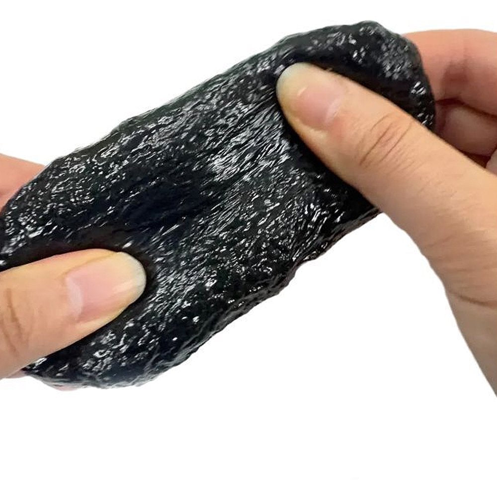 Both hands pulling and stretching a dark charcoal Stone Crunch Squishy Slime Toy revealing a bumpy rock-like surface and dense ASMR crunch beads for tactile anxiety relief
