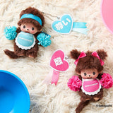 Two Monchhichi plush toys with blue and pink accessories on a white fluffy surface.