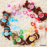 Monchhichi dolls with various accessories on a textured surface