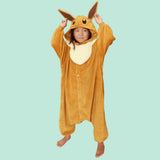 Official Pokémon Eevee Kids Costume Kigurumi Onesie Jumpsuit worn by a young model holding the pointed long ears. Features a soft light-brown fleece body, fluffy cream collar fluff, and an Eevee character face hood. Perfect for kids' Halloween costumes, cosplay party suits, sleepovers, and birthday gifts