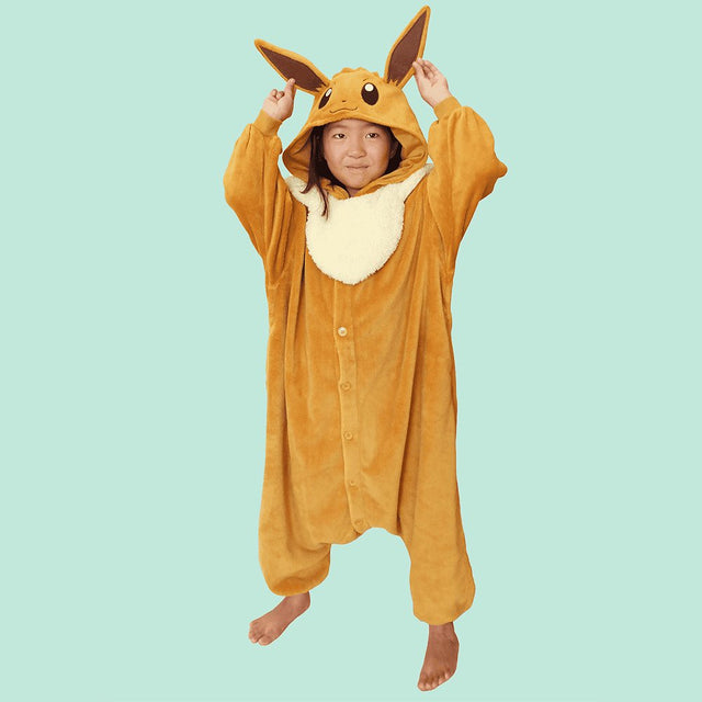 Official Pokémon Eevee Kids Costume Kigurumi Onesie Jumpsuit worn by a young model holding the pointed long ears. Features a soft light-brown fleece body, fluffy cream collar fluff, and an Eevee character face hood. Perfect for kids' Halloween costumes, cosplay party suits, sleepovers, and birthday gifts