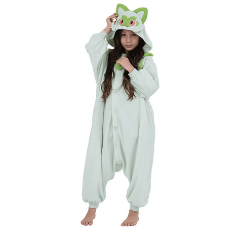 Official Pokémon Sprigatito Kids Costume Kigurumi Onesie Jumpsuit worn by a smiling young model holding the hooded ears. Features a soft pale mint-green fleece body, green leaf collar, and a Sprigatito face hood with pink eyes. Ideal for kids' Halloween costumes, cosplay party suits, sleepovers, and holiday gifts