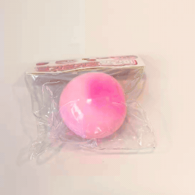 Hands squeezing a soft pink Strawberry Rice Cake Bread Squishy Toy through its clear plastic packaging, demonstrating squishy elasticity and doughy feel for fidget lovers and holiday gift guides