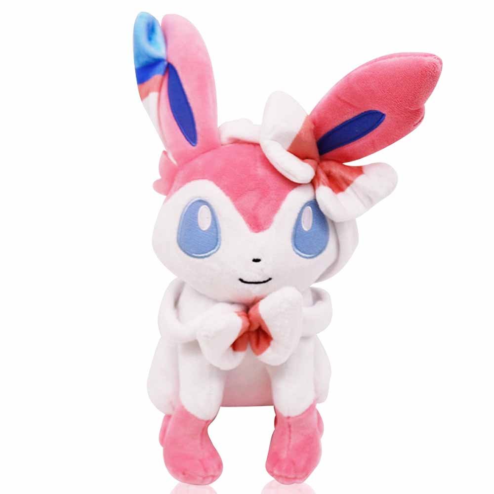 A plush toy depicting the Pokemon Sylveon, primarily white with pink and blue accents, sitting with its hands clasped.